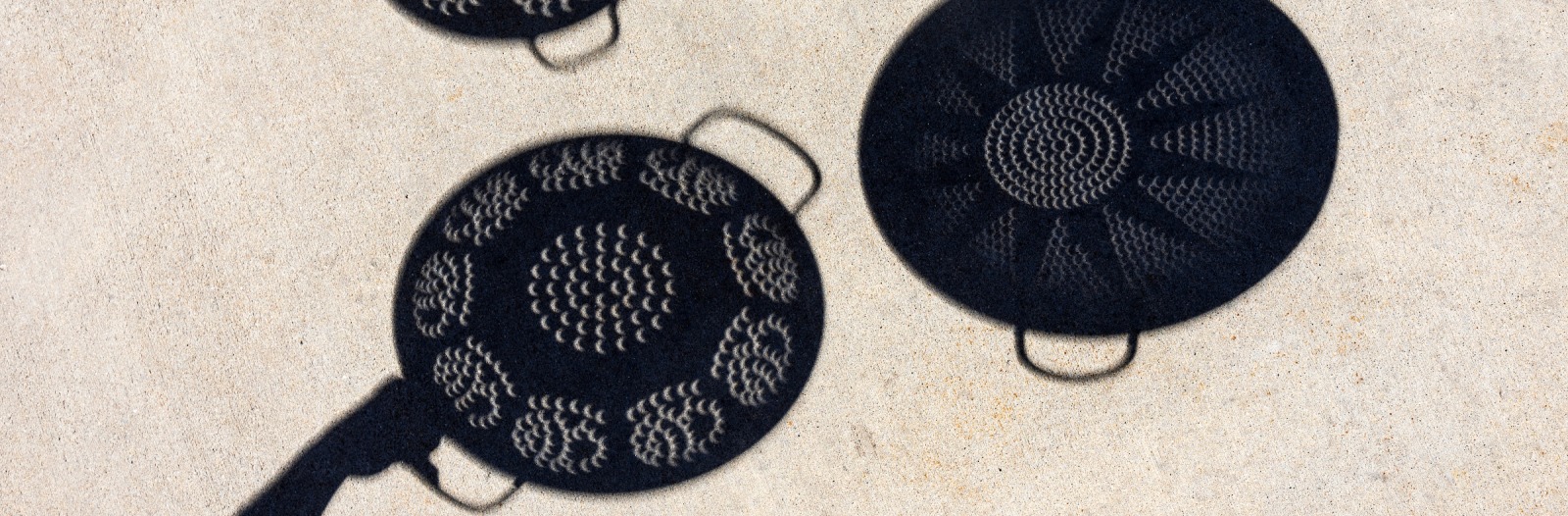 Shadows of colanders on the sidewalk working as pinhole cameras to view the shadow of the moon crossing the sun