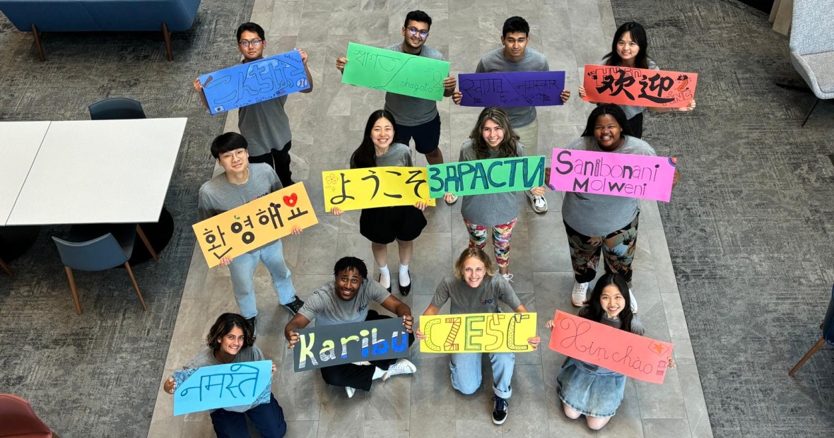 Several people hold up signs with "welcome" written in different languages and smile up at the viewer