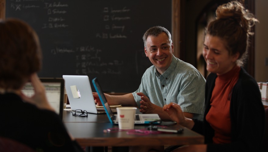 A smiling professor works with two research students. 