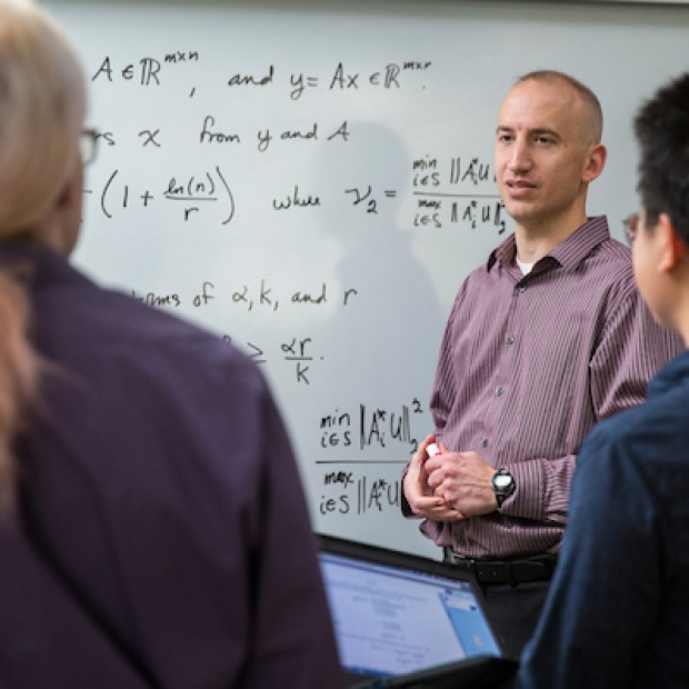 Two students work at whiteboard with professor