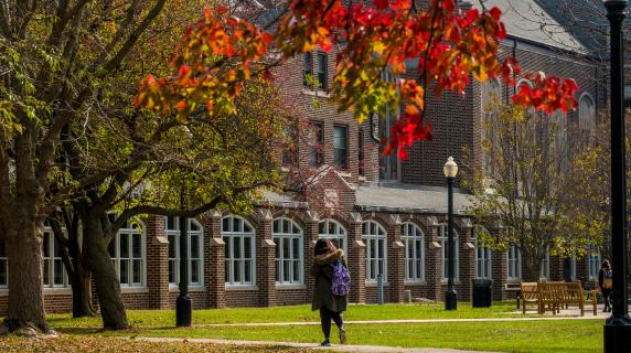 student walks near South Campus residence halls, autumn leaves in foreground