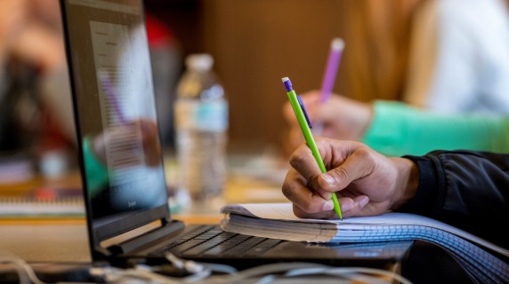 Someone writing on paper with laptop in front of them