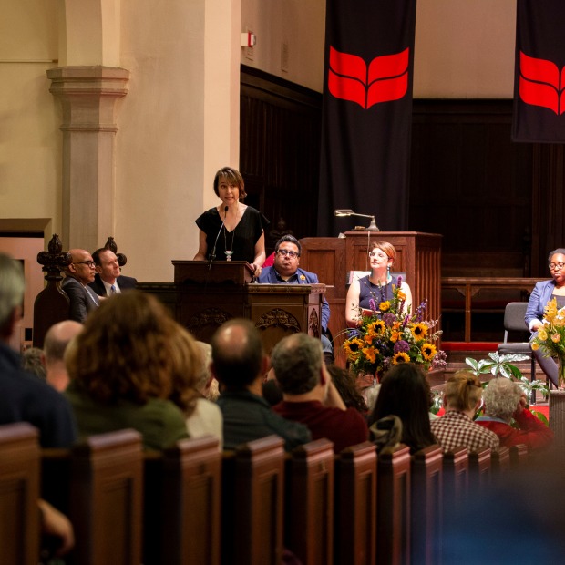 Speaker at podium in Herrick Chapel speaking to seniors and guests, laural leaf banners in the background