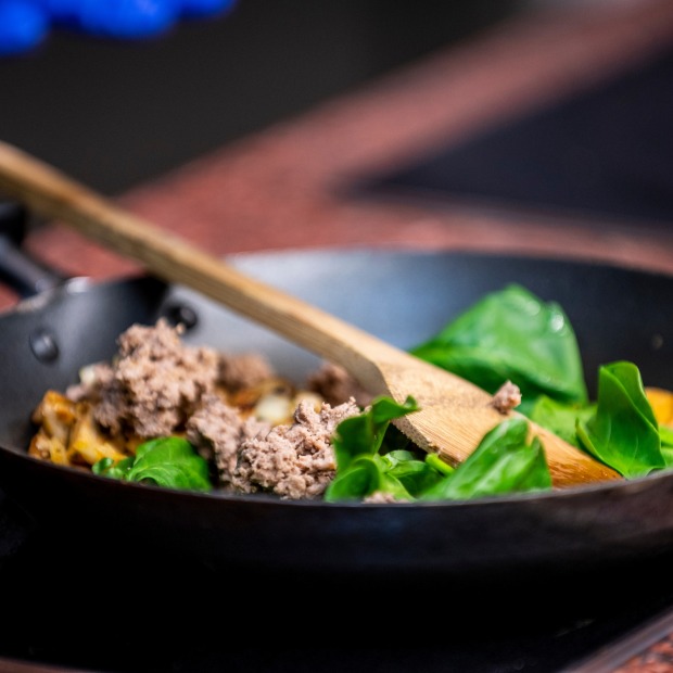 A small saute pan with fresh spinach leaves and ground meat, ready to be tossed together