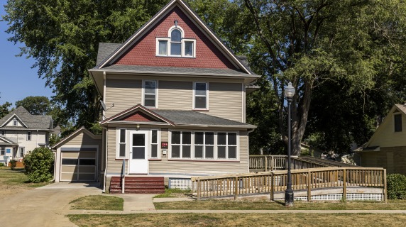 2 and a half story tan house with red upper story and an access ramp wrapping around to the right.