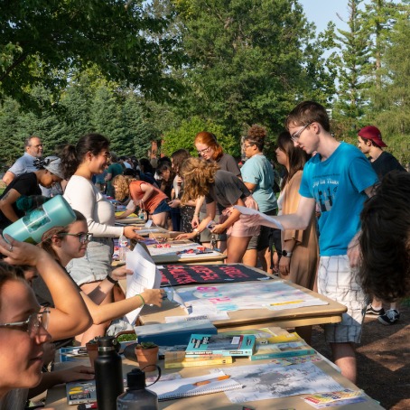 A student organization fair. Two young men ask the representatives about their clubs/organizations.