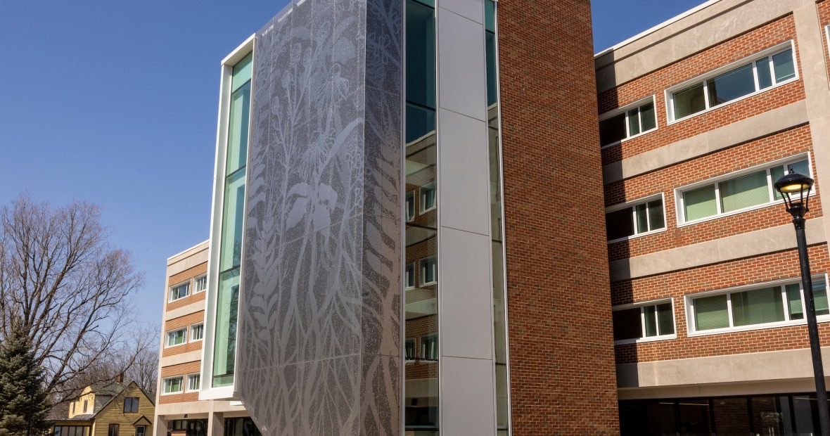 4 story brick building with large windows and a decorative perforated steel panel with prairie plants the height of the building