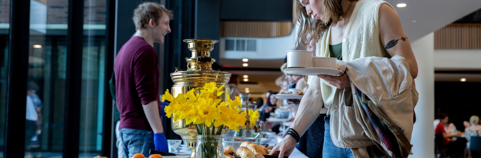 one person serving food and the other getting it with yellow flowers in the background 
