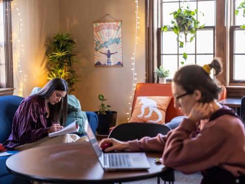 two people studying on couches and at a table with windows in the back