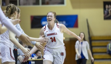 A young woman basketball player runs past a lineup of her teammates, high fiving everyone