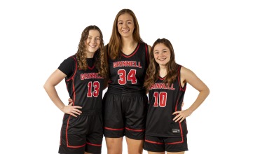 Three young women in basketball uniforms stand arm in arm