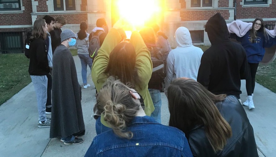 Students gathered around the base of Gates Tower view the sun shining through the arch.