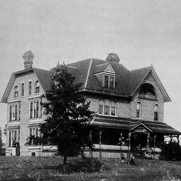 Historic black and white photo of Mears Cottage with women sitting on the porch, steps and lawn