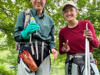 Mia and her friend have hiking gear on and smile at the camera