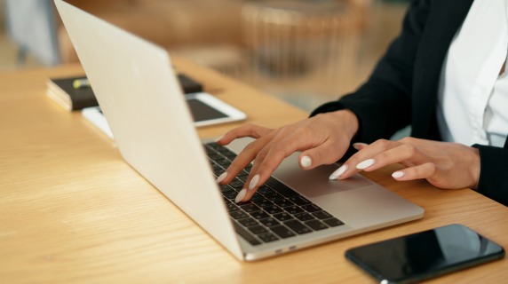 An applicant applies for a job using a laptop computer. Mobile phone and tablet are sitting on the table next to the laptop.