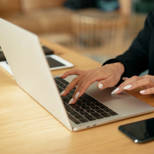 An applicant applies for a job using a laptop computer. Mobile phone and tablet are sitting on the table next to the laptop.
