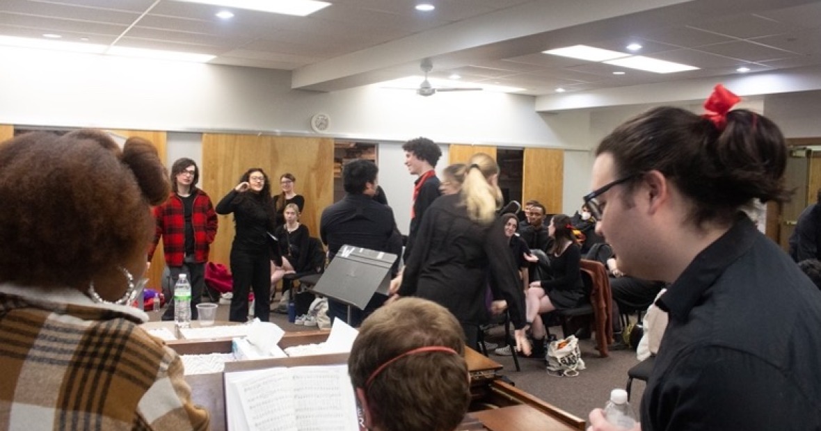 A group of people in black mindle in a large room with a pianist sitting with back to the camera in the foreground