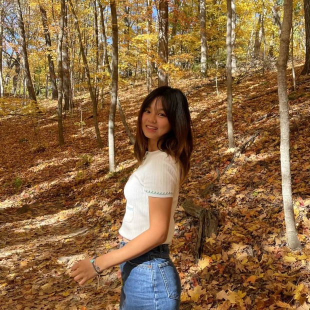 Betty standing to the left and turning to look at the viewer, surrounded by trees in autumn