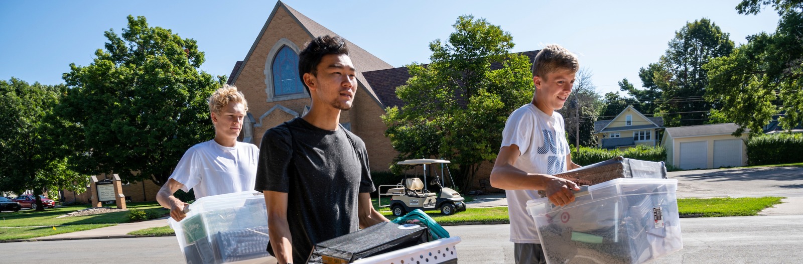 Three students carrying boxes of belongings, excited to be moving in