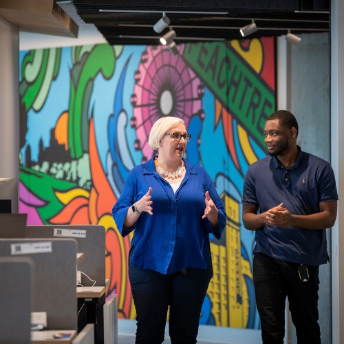 Carlton Segbefia and a co-worker talk as they walk past a colorful mural