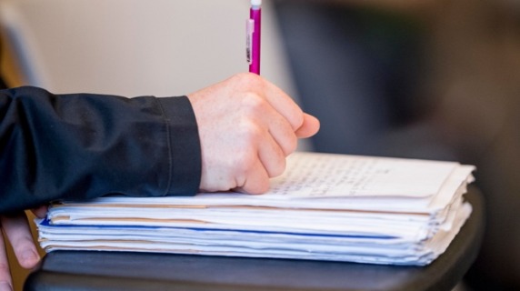 Hand with pen writing on stack of paper