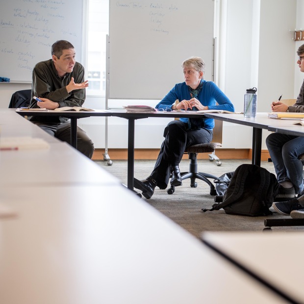 A faculty member speaks to a group of students gathered around a table