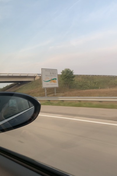 The "Welcome to Iowa" sign as seen through a car window