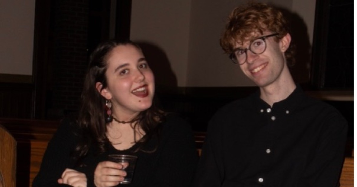 Two people in black clothes sit on a wood pew