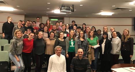 4 rows of students of the Grinnell Singers are stacked in Bucksbaum lecture room 152. John Rommereim and Syrian-American composer Kareem Roustom sit down in front of the students