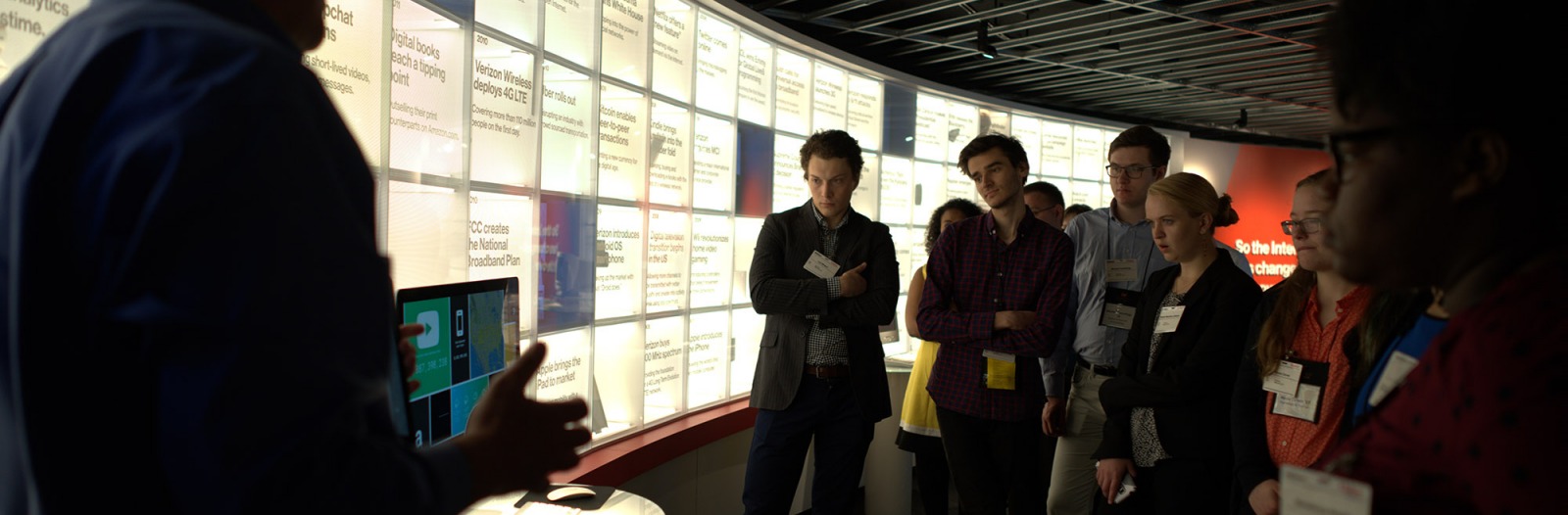Students stand in front of monitors listening to an alumnus