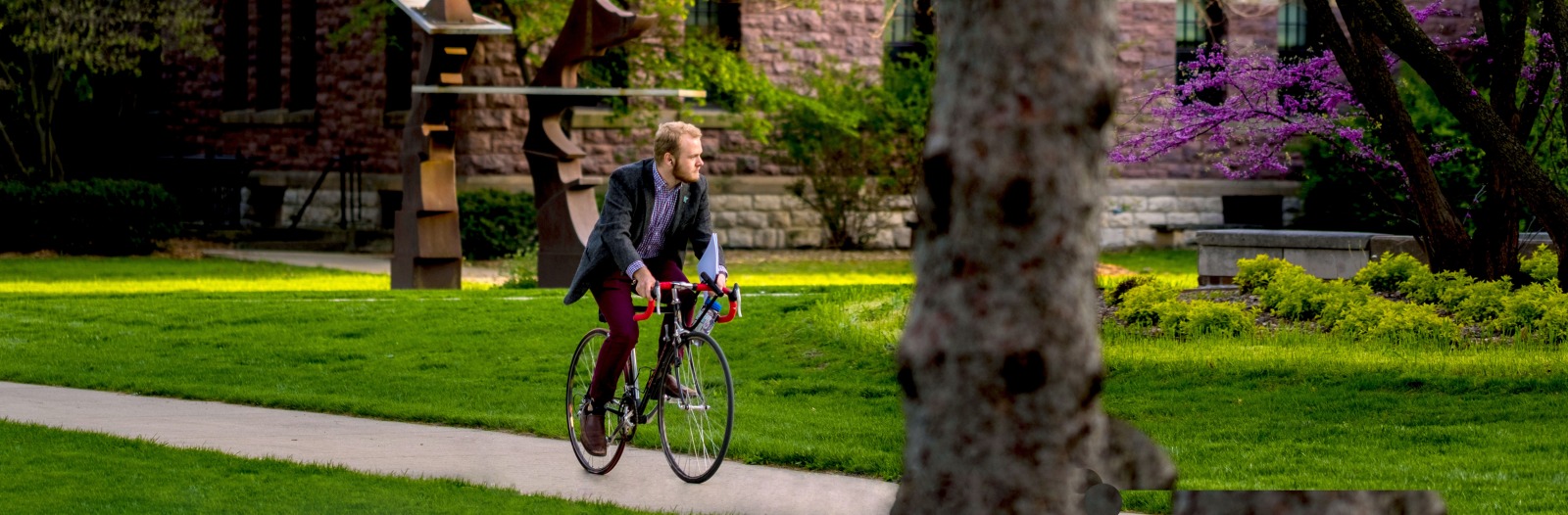 Student bikes past campus sculpture near Goodnow Hall on a beautiful spring day
