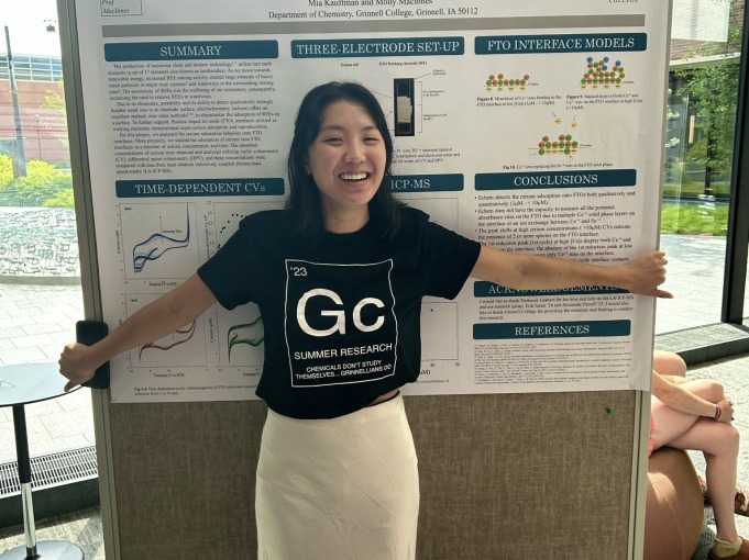 Mia is in front of her MAP presentation billboard. She smiles happily at the camera with her research behind her.