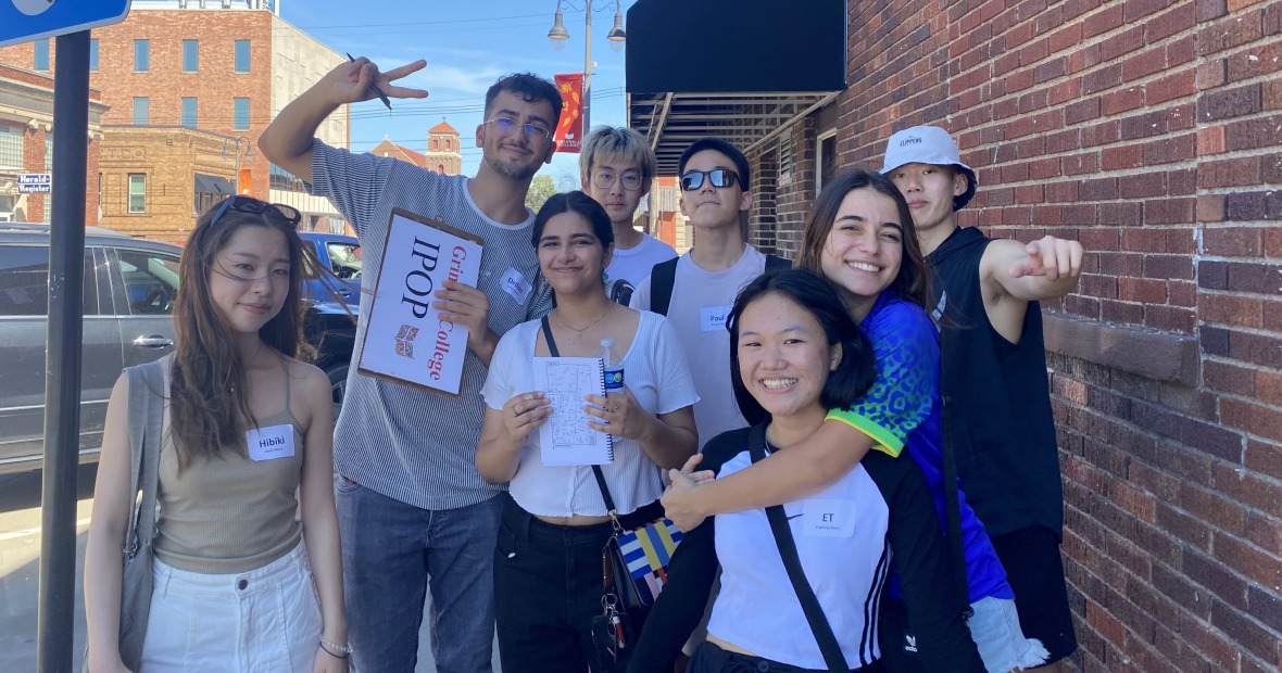 Small group of students standing next to a brick building, smiling at the camera