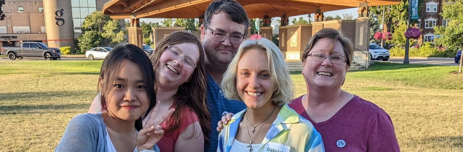 Family of three stands in the park with two students
