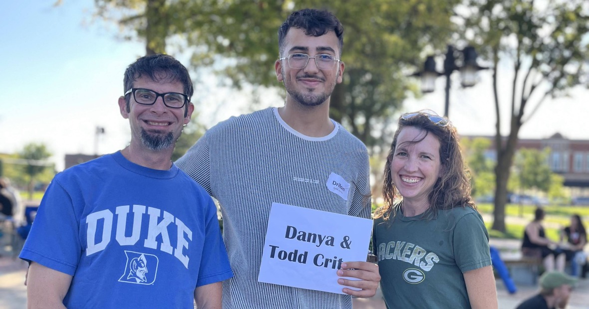 Three people stand in a park and smile at the viewer