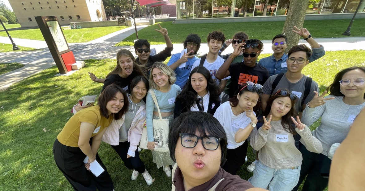 Large group of students standing together smiling at the viewer and making peace signs with their hands