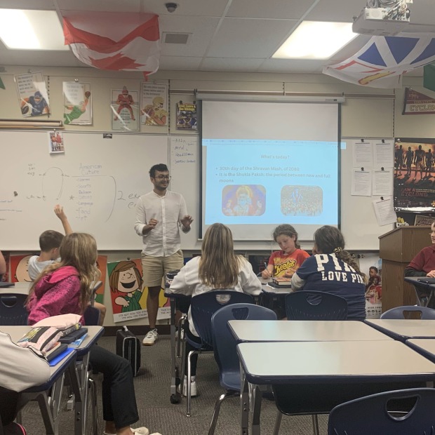 Parikshit stands next to a large screen in front of a classroom of students sitting at desks