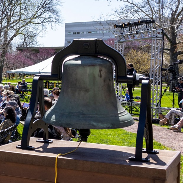 Iowa College Bell in the foreground, with an audience at the commencement stage behind it