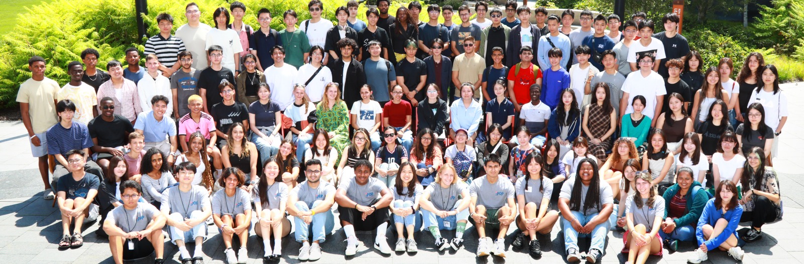 A large group of people standing outside in a grey courtyard, smiling at the viewer