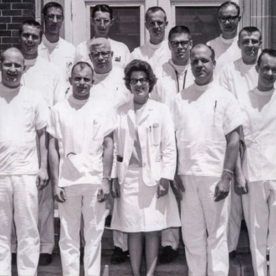 JoEllen Hoth and twelve other doctors in white scrubs stand on the front step of a hospital.