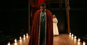 A performer in a red cloak treads between period-style footlights