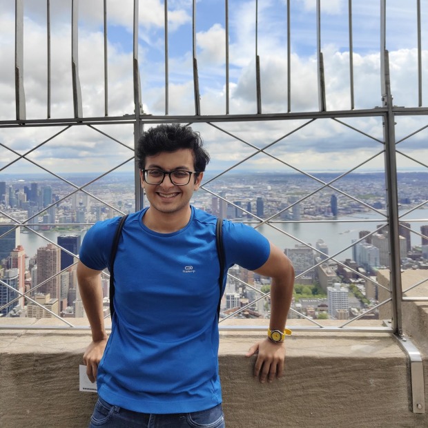 Parikshit stands in front of a vast city landscape, smiling at the viewer