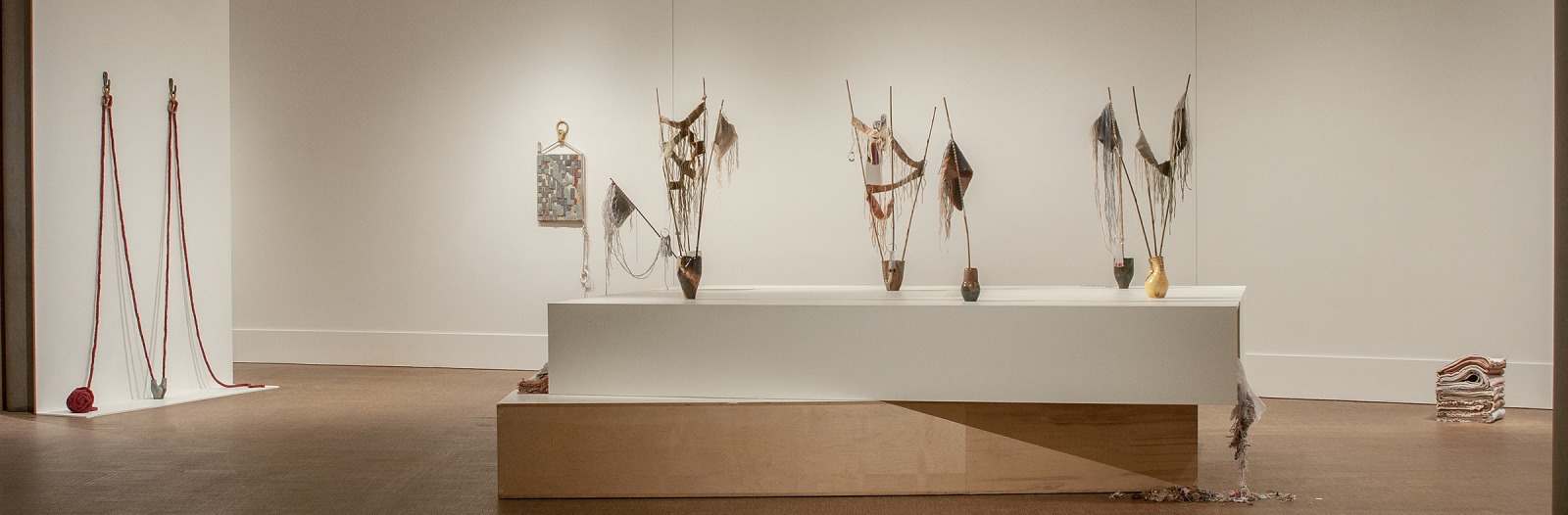 Installation view of Jeremy Laing's ceramic vases with bamboo poles and swatches of fabric emerging from them.