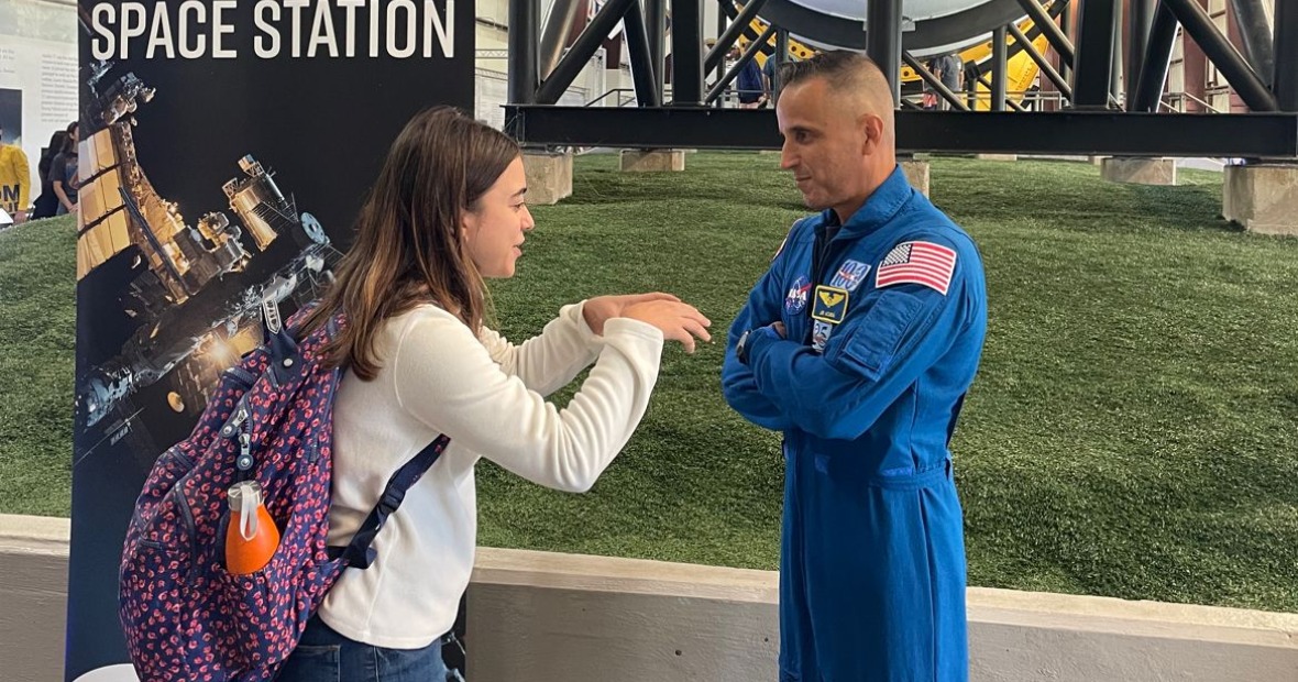 Sophia animatedly talks to an astronaut beneath a rocket display. 