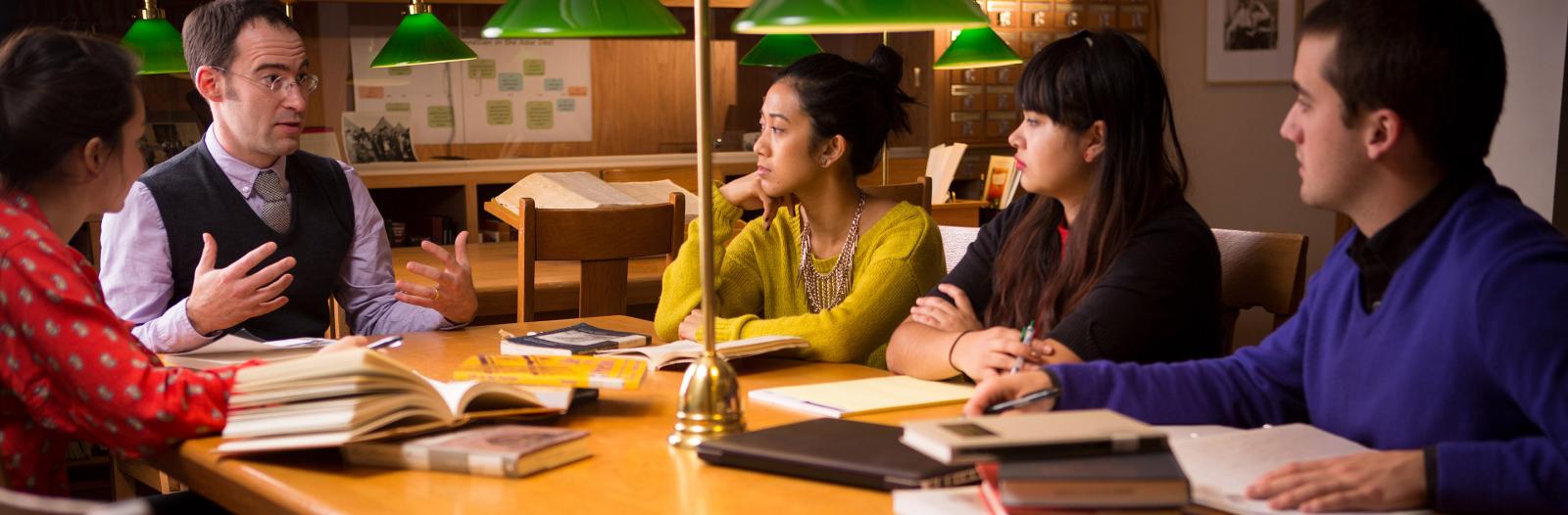Caleb Elfenbein, Assistant Professor of History and Religious Studies meets with a small group of students in the Iowa Room in the basement of Burling Library