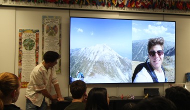 Two students present. A TV screen displays a Bulgarian landscape and a selfie from a presenter.