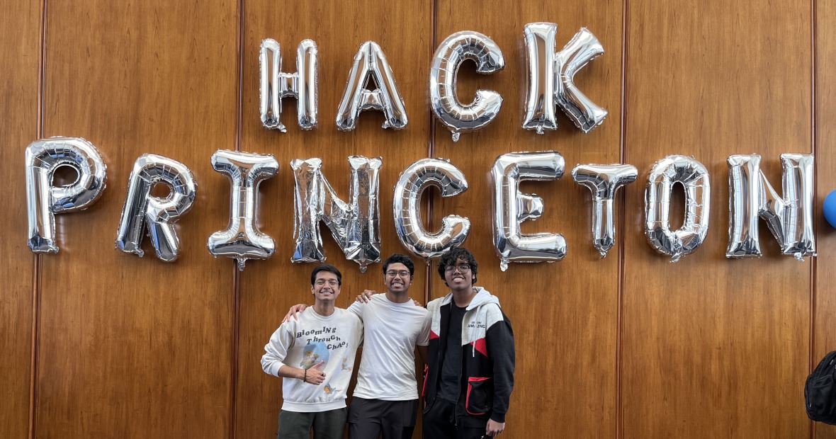 Three students pose below the Hack Princeton banner made with inflated mylar ballons. 