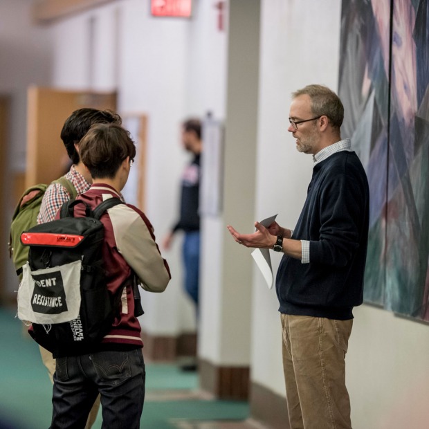 Students talk to older adult in hallway