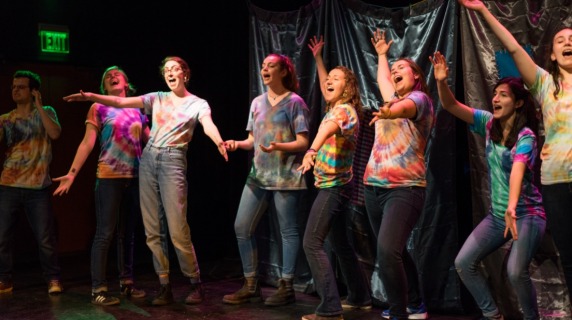A group of students in bright clothing sing enthusiastically