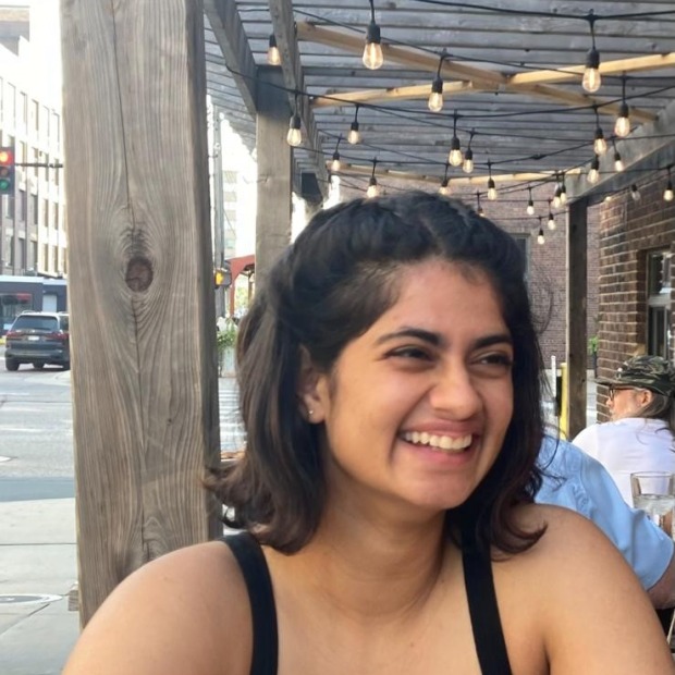 Utsah sits outside with hanging lights above her head, and smiles while looking to the right